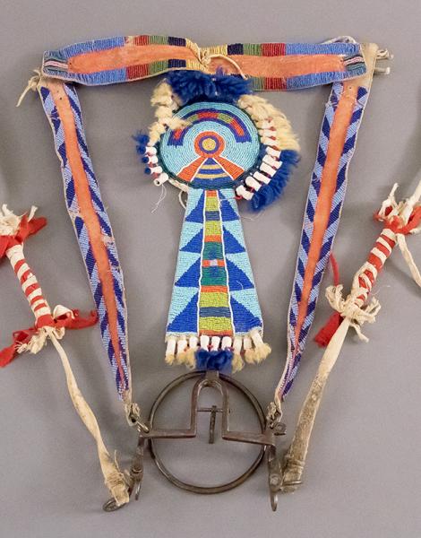 Central rosette and tab suspension, fully beaded in geometric motifs, wool tuft suspensions, fastened to red-dyed and edge-beaded brow and cheek bands, with metal bit and hip strap reins.